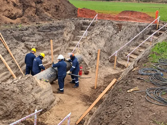 Crew in hard hats working on an exposed pipeline in a marked-off excavation.