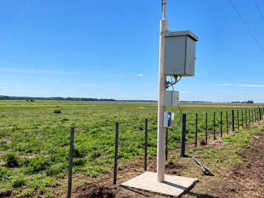 Rectificador de protección catódica montado en su poste, junto a un alambrado en el campo.