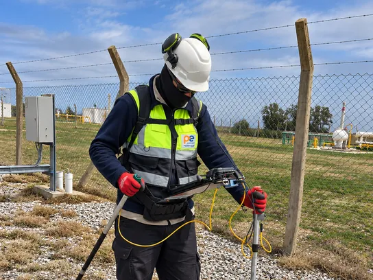 Técnico con EPP completo recorre la traza con los electrodos y el registrador de datos al pecho.