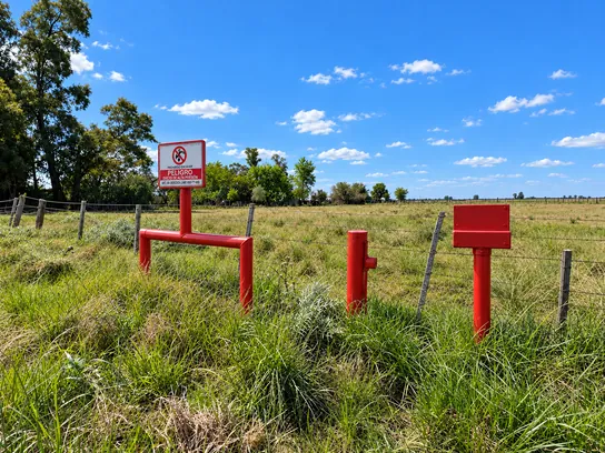 Mojón, venteo y cartel de peligro sobre la traza de un ducto de alta presión, en el campo.